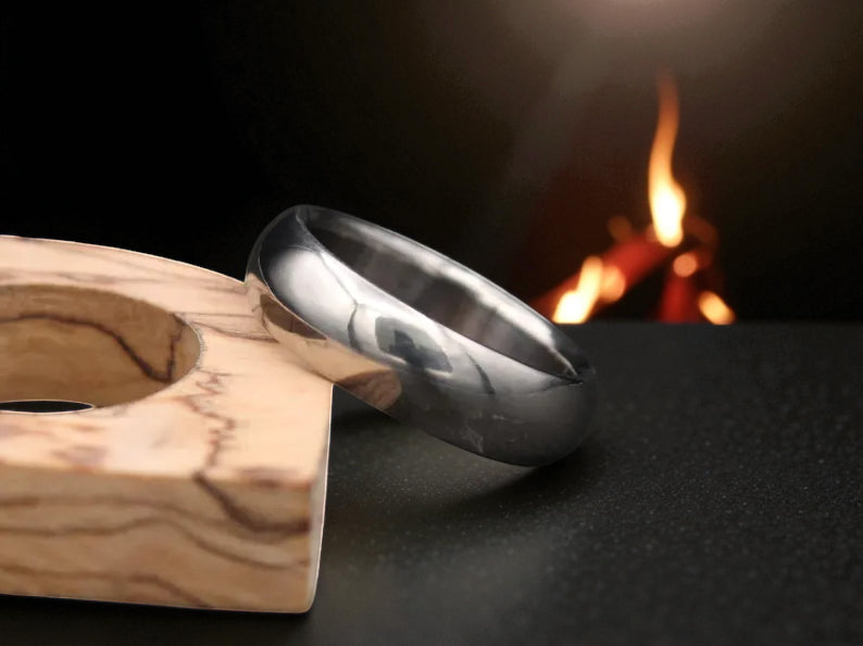 Polished titanium dome-shaped ring with brushed finish beside wooden accent
