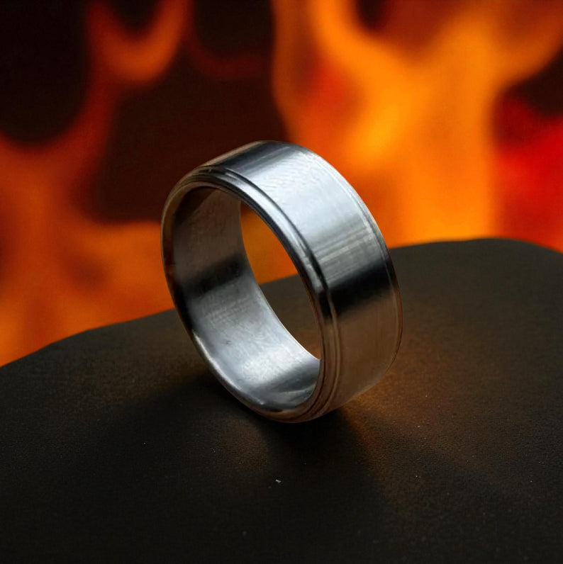 Brushed titanium ring on dark surface with fiery background