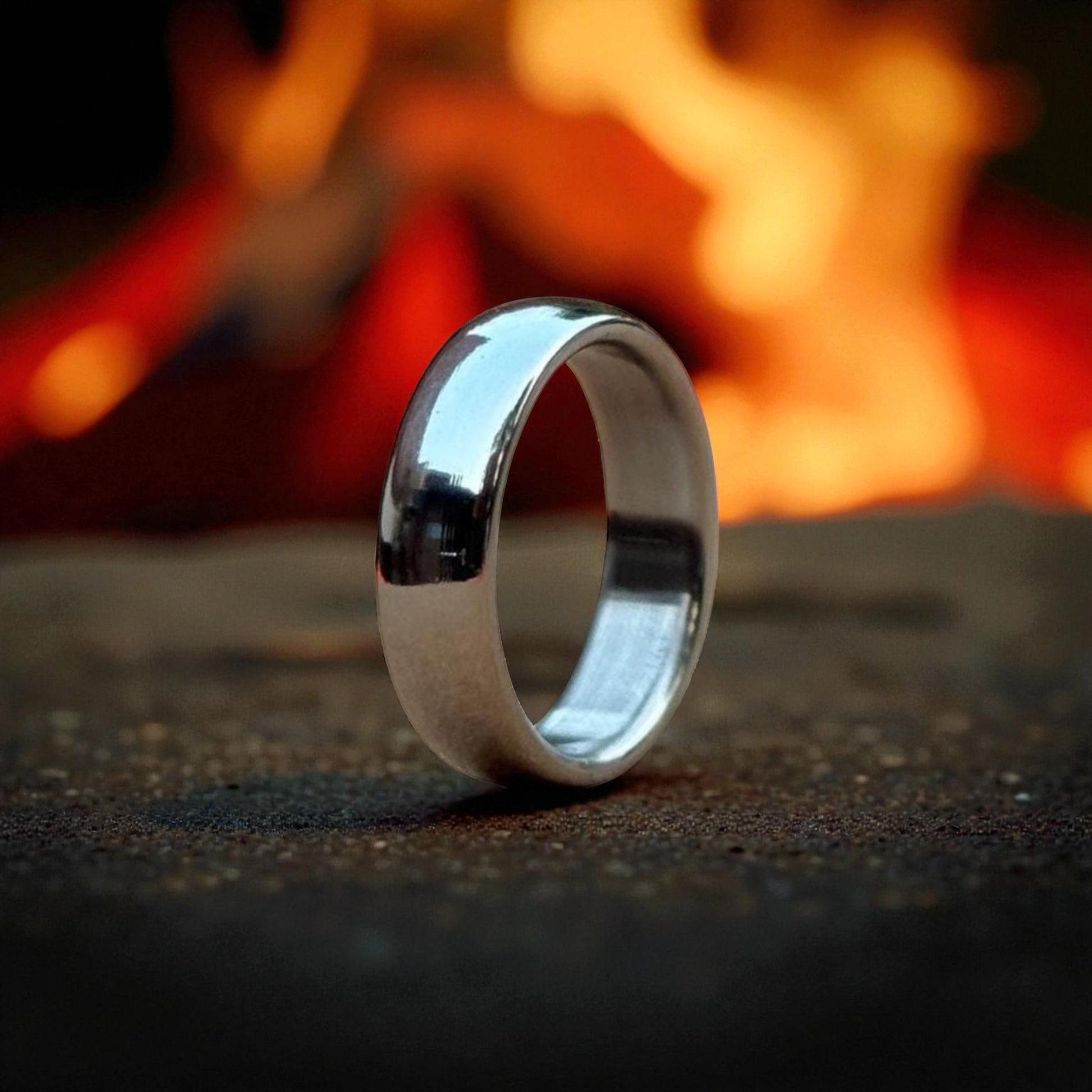 A titanium polish finish dome-shaped wedding ring rests on a table, illuminated by the warm glow of a nearby fire.