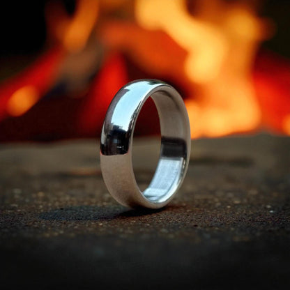 A titanium polish finish dome-shaped wedding ring rests on a table, illuminated by the warm glow of a nearby fire.
