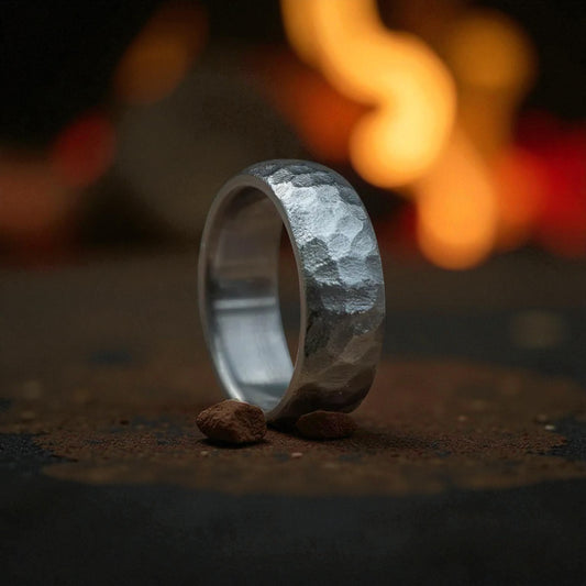 A close-up of a titanium rock hammered curved wedding ring placed on rugged rocks, highlighting its craftsmanship and beauty.