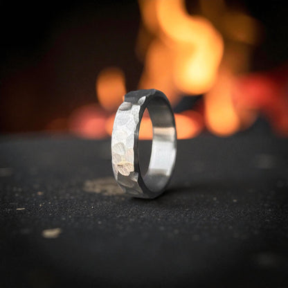 A silver Titanium Rock Hammered Curved Ring displayed atop dark, rough rocks.