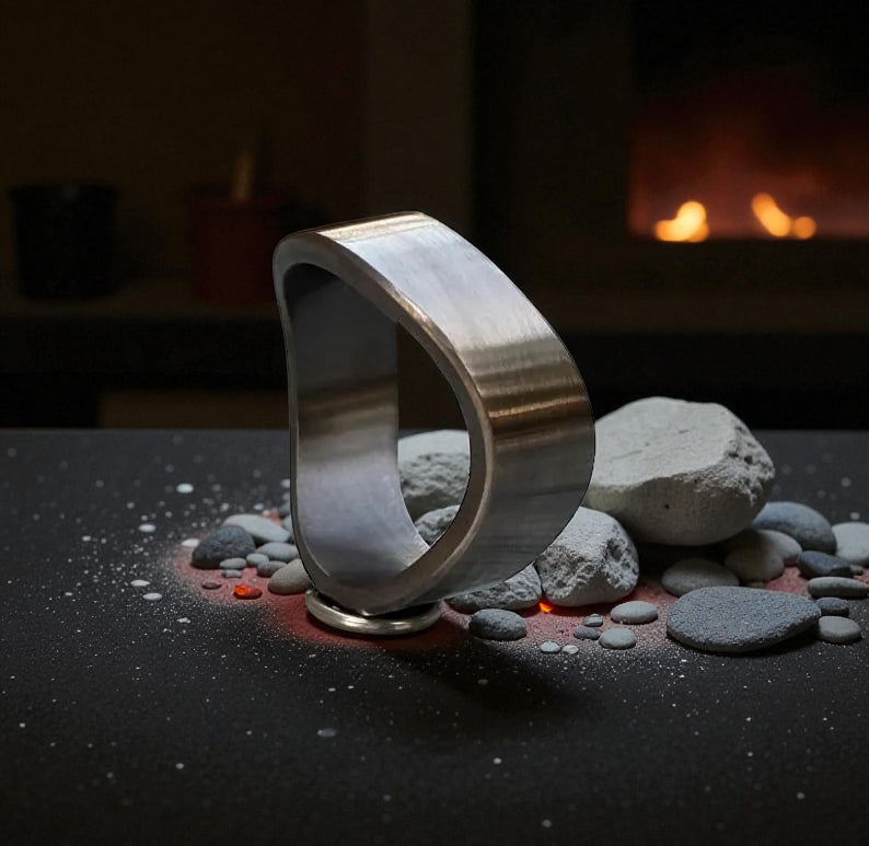 Close-up of asymmetrical brushed titanium ring with warm firelight background