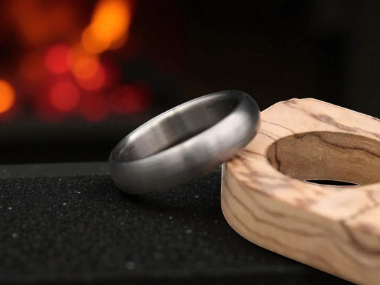 Brushed titanium dome-shaped ring resting beside a wooden circle accent