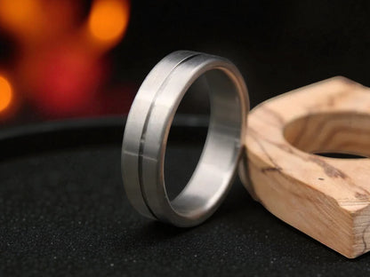 Titanium brushed groove ring resting beside wooden accent, featuring matte texture and center groove