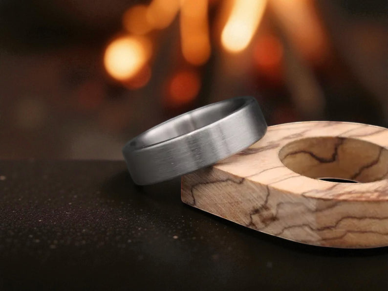 Titanium brushed finish ring placed beside wooden accent block with blurred fire background
