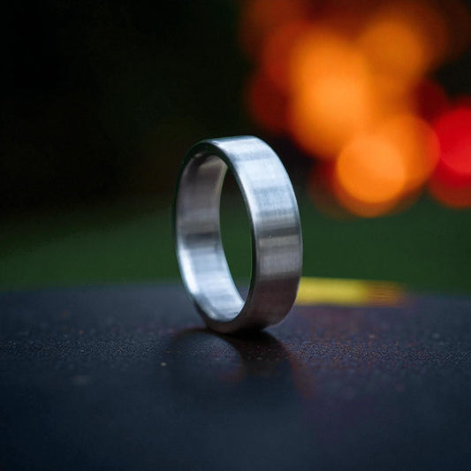 Titanium ring with brushed matte finish on a dark surface, glowing firelight background