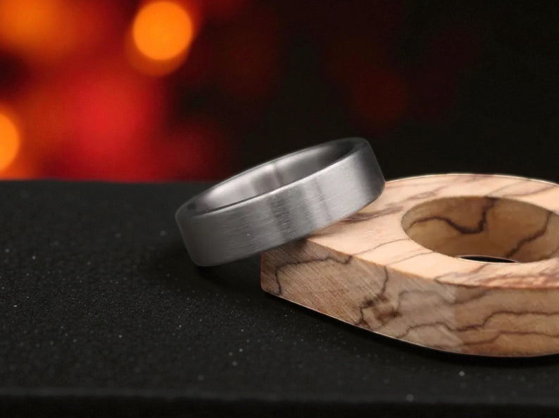 Close-up of matte titanium ring with soft brushed surface, warm ember tones behind