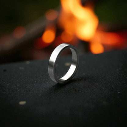 Close-up of matte titanium flat ring with brushed surface resting on dark textured surface