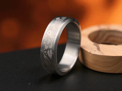 Titanium ring with deep floral engravings placed beside a wooden accent on a black surface, warm bokeh fire background