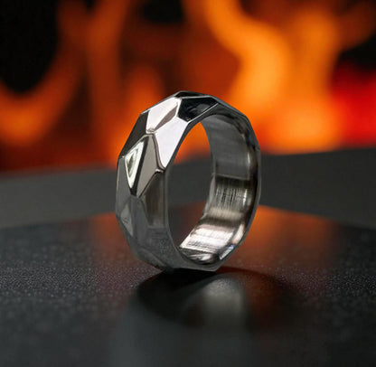 Titanium ring with diamond-cut facets and high-polish finish on a dark matte surface, warm fire background