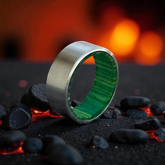 Titanium ring with brushed silver exterior and green whiskey barrel wood interior, placed on black stones and glowing embers