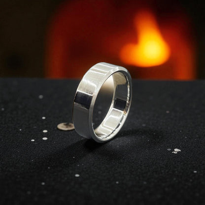 A shiny titanium wedding ring is placed on a table, with a soft fire casting light around it.
