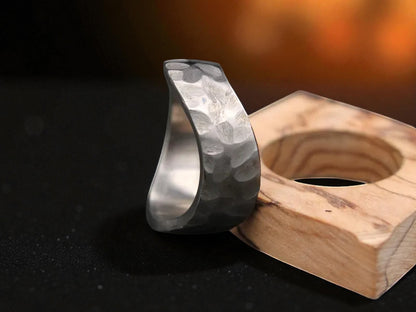 A titanium ring with a hammered metal band displayed on a wooden block, showcasing its unique curved design.