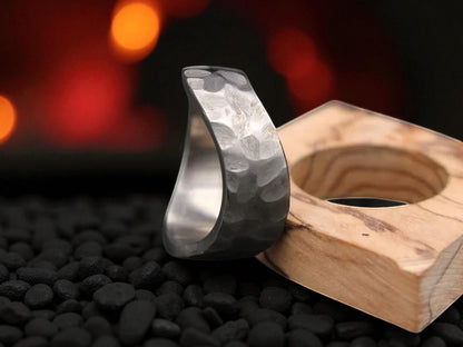 A close-up of a titanium hammered ring resting on a wooden block, highlighting its elegant curved shape.