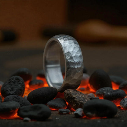 A titanium curved wedding ring with a hammered finish, elegantly positioned atop a bed of rough rocks, emphasizing its style.