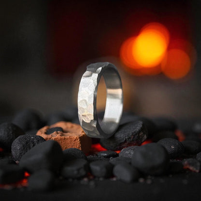 Close-up of a silver Titanium Rock Hammered Curved Ring on a bed of black stones.