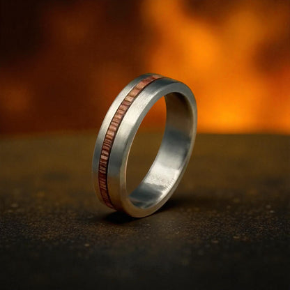 Wedding ring with a copper inlay resting on rocks, showcasing a unique Titanium Whiskey Barrel design.