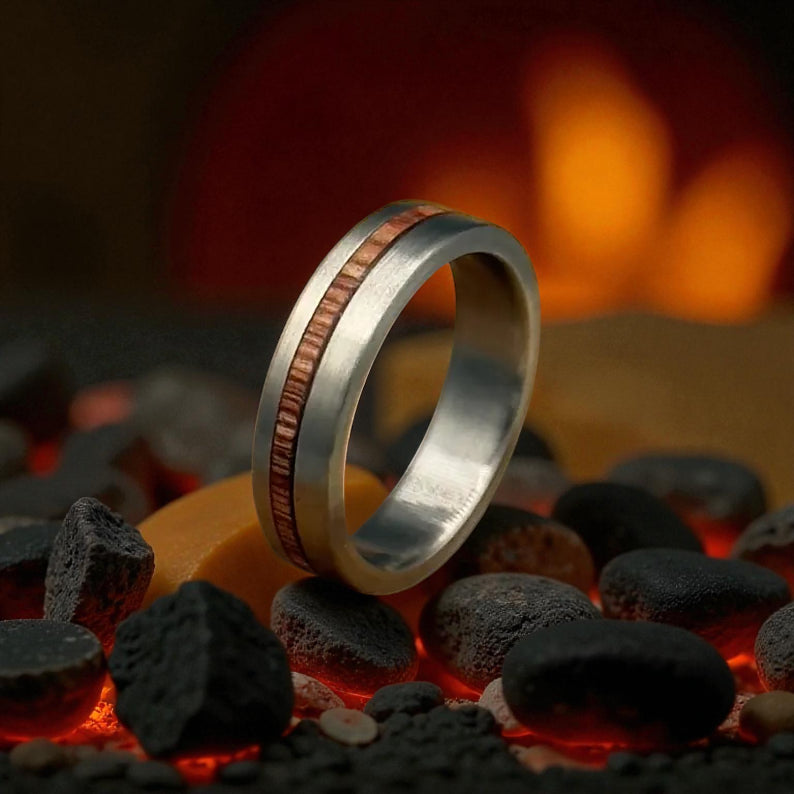 A Titanium Whiskey Barrel wedding ring with a copper inlay displayed on rugged rocks, highlighting its distinctive design.