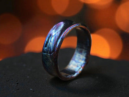 Curved titanium ring with blue and violet hues on dark textured surface