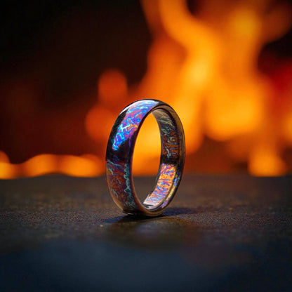 Dome-shaped titanium ring with iridescent blue finish on dark surface