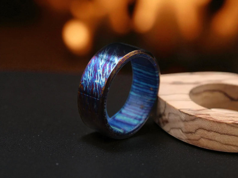 Blue titanium ring with whiskey barrel wood interior on dark surface