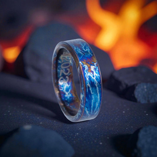 Flat titanium ring with electric blue lightning pattern on dark rocky surface